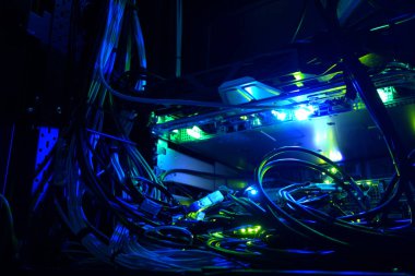 A vibrant and intricate view of network cables and server equipment illuminated in blue light, showcasing the complexity of modern technology in a dark setting.