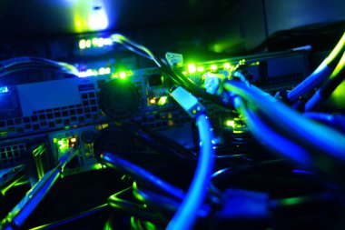 Sunucu odasındaki renkli kabloların ve parlayan ışıkların yakın görüntüsü. Görüntü, teknolojinin ve ağ sistemlerinin özünü yakalıyor. Detaylı kablolama ve aydınlatılmış bağlantıları gösteriyor..