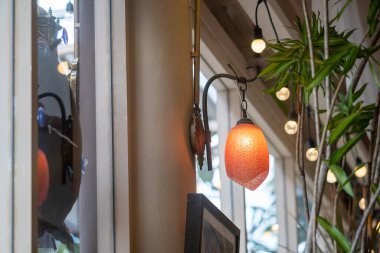 Çok güzel tasarlanmış bir lamba, sıcacık bir kafe ortamında asılı duruyor, sıcak bir ışık saçıyor. Zarif cam parçaları ve çevreleyen bitkiler sakin bir atmosfer yaratıyor..