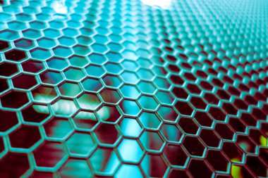 Karmaşık bir altıgen metal ağ deseninin yakın çekimi canlı renkler ve yansıtıcı yüzeyler sergiliyor, modern tasarım ve endüstriyel temalar için mükemmel..