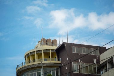 Parlak mavi gökyüzüne ve bulutlara karşı su tankları olan modern bir bina. Görüntü şehir mimarisi ve eşsiz tasarım elementlerini sergiliyor.