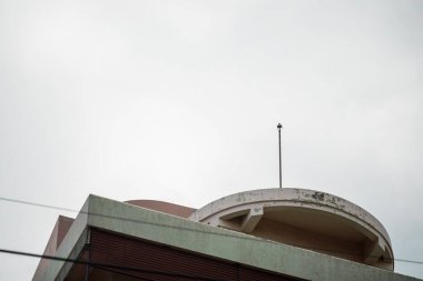 Bulutlu bir gökyüzünün altında eşsiz bir çatı tasarımına sahip modern bir bina. Mimari detaylar çağdaş kentsel estetik ve minimalizmi vurguluyor.