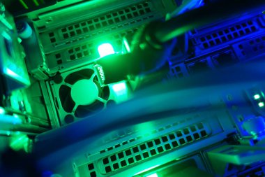 Yüksek teknolojili sunucu odasına yakın çekim. Işıklı yeşil ışıklar, soğutma vantilatörleri ve karmaşık ağ kabloları. Gelişmiş teknoloji sergileniyor..