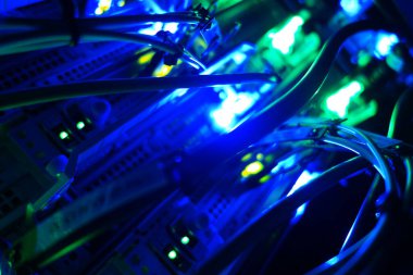 Ağ ekipmanları arasında parlayan canlı mavi ışıkların yakın çekimi, dijital altyapı ve bağlanabilirliğin karmaşık tasarımı ve teknolojisini gözler önüne seriyor.