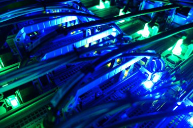 Aydınlatılmış sunucular ve canlı kablolar sergilenen modern bir veri merkezinin yakın plan görüntüsü. Mavi ve yeşil ışıklar ileri teknoloji ve bağlantıyı vurguluyor..