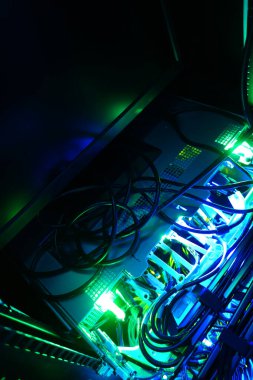 Teknoloji rafında mavi ve yeşil ışıkta aydınlatılan sunucu kablolarının canlı bir görüntüsü, modern altyapı ve elektronik bağlantıları sergiliyor..