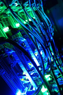 Canlı mavi ve yeşil ışıklarla aydınlatılan sunucu kablolarının soyut bir görüntüsü, yüksek teknoloji ortamlarının tipik modern ve dijital atmosferini sunuyor.