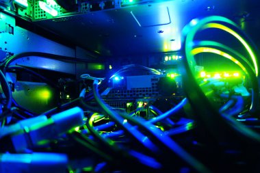 Sunucu rafındaki canlı mavi ve yeşil ışıklarla aydınlatılan renkli ağ kablolarının karmaşık bir görüntüsü, modern teknoloji ve bağlantıyı sergiliyor.