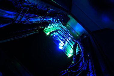 Karanlık bir ortamda aydınlatılmış sunucu bağlantı kablolarının yakın görüntüsü. Canlı mavi ve yeşil ışıklar gelişmiş teknolojiyi ve organizasyonu vurguluyor..