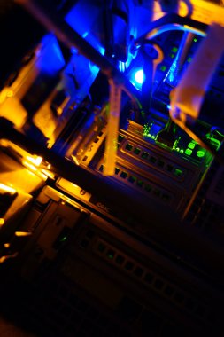 Bu resim bir sunucu odasının karmaşık düzenini gösterir. Parlayan ışıklar ve kablolar modern veri işleme teknolojisinin elektronik manzarasını gösteriyor.