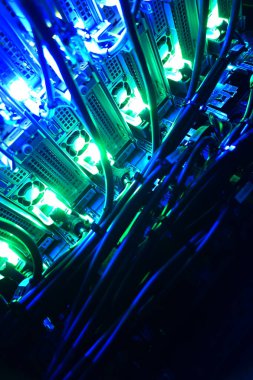 Çeşitli donanıma bağlı karmaşık kabloları aydınlatan canlı mavi ve yeşil ışıkları gösteren bir sunucu rafının yakın plan görüntüsünü keşfedin.