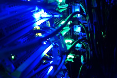 Parlak mavi ışıklar ve karmaşık kabloların yer aldığı aydınlatılmış sunucu raflarının yakın görüntüsü, modern teknoloji ve veri altyapısını eylem halinde gösteren.