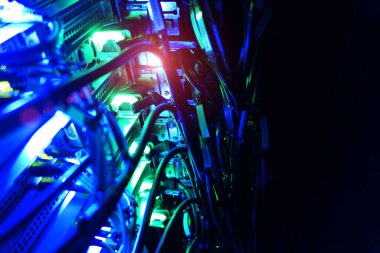 Canlı bir sunucu odasında mavi ve yeşil kablolar aydınlatılıyor. Görüntü, teknolojinin karmaşık düzenini, bağlantıyı ve modern tasarımın altını çiziyor..