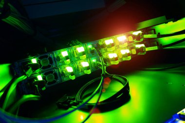 Aydınlatılmış ağ sunucu bileşenlerinin karanlık bir ortamda yakın plan görüntüsü, canlı yeşil ışıklar, kablolar ve eylem halindeki teknolojiyi gösteriyor.