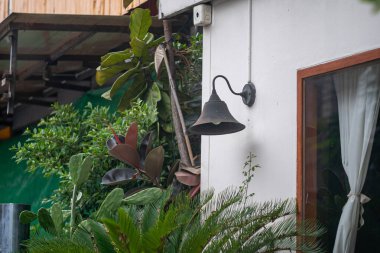 Yeşillikler arasında bir duvara monte edilmiş bir kırsal çan, dış uzaya cazibe katarak konumun davetkar atmosferini artırıyor..