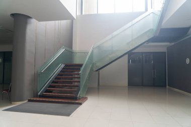 Modern cam merdiven parlak bir lobide çarpıcı bir odak noktası oluşturur, zarafet ve işlevselliği geniş bir iç tasarımda birleştirir..