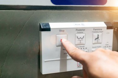 Durdurma düğmesi de dahil olmak üzere çeşitli düğmelerden oluşan bir bidet kontrol panelinin yakın çekimi. Görüntü, kişisel hijyen için kontrole basan bir eli yakalar..