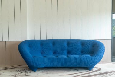 Çağdaş ev tasarımlarını geliştirmek için mükemmel, eşsiz bir şekil ve dokuya sahip minimalist bir iç dekora yerleştirilmiş çarpıcı bir modern mavi kanepe..