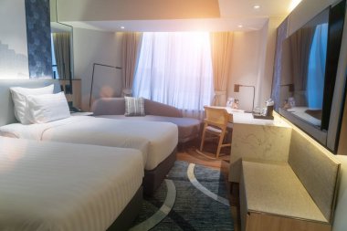 Bu resim, rahat bir dekorun, rahat bir yatağın ve parlak doğal ışığın bulunduğu modern bir otel odasını sergiliyor. Konuklar için rahatlatıcı bir atmosfer yaratıyor..