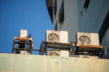 Bu görüntü, açık mavi gökyüzünde endüstriyel makineleri gösteren bir binanın çatısındaki havalandırma ünitelerini yakalıyor. Kentsel ortamları resmetmek için ideal.