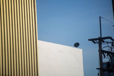 Açık mavi gökyüzüne karşı zıt bina yüzeylerine sahip modern mimarinin soyut görüşü, canlı bir şehirde kentsel tasarım unsurları ve yapısal çizgiler sergiliyor.