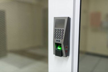 Modern bir biyometrik parmak izi tarayıcısı girişe yakın bir yerde. Cihaz başarılı bir erişim gösteren bir tuş takımı ve yeşil bir sinyal içeriyor.