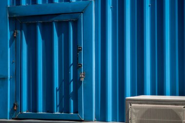 Parlak mavi bir kapı, dokulu bir duvara dayanır ve çarpıcı bir görsel karşıtlık yaratır. Işık ve gölge, sahnenin endüstriyel çekiciliğini arttırır.