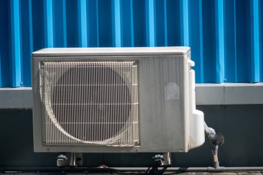 Mavi bir bina duvarına monte edilmiş açık hava klima ünitesini gösteren detaylı bir görüntü. Fotoğraf, kentsel ortamlarda HVAC ekipmanlarının temel özelliklerini vurguluyor.