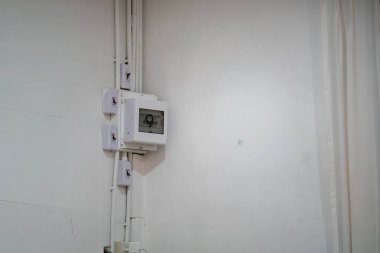 Termostat ve görünür kablolardan oluşan minimalist beyaz bir duvar, basit bir iç mekanda modern ev teknolojisi ve enerji yönetimini gösteriyor.