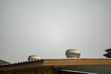 Endüstriyel bir çatıdaki metal türbin havalandırma sistemlerinin görüntüsü modern tasarım ve verimli hava dolaşımını gri gökyüzü arka planına karşı sergiliyor..