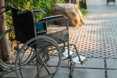 Boş bir tekerlekli sandalye kaldırımda, doğa ile çevrili, kentsel alanlarda hareketlilik ve ulaşılabilirlik temalarını vurgulayan barışçıl ama dokunaklı bir sahne yaratıyor..