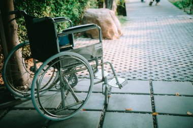 Manzaralı bir bahçe yolunun kenarına yerleştirilmiş boş bir tekerlekli sandalye, hareketlilik, ulaşılabilirlik ve doğa ile insan deneyimi arasındaki huzurlu bağlantıyı vurguluyor..