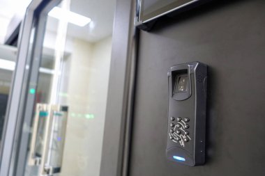 Duvara monte edilmiş modern bir erişim kontrol sisteminin yakın plan görüntüsü, güvenli giriş için biyometrik bir parmak izi okuyucusu ve tuş takımı içeriyor.