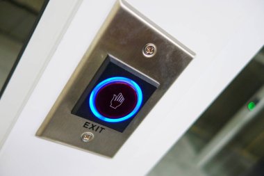 Bir el sembolü ile modern aydınlatma çıkış düğmesinin yakın plan görüntüsü, bina ortamında işlevselliğini ve kullanıcı dostu tasarımını gösteriyor.