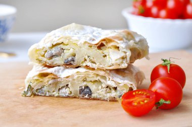 Ev yapımı tavuk turtası. Tavuk eti ve mantarla doldurulmuş taze lezzetli turta. Tahta tabakta servis ediliyor, domates kirazlı..