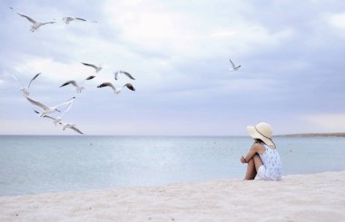 Şapkalı küçük tatlı kız sahilde martıları besliyor..