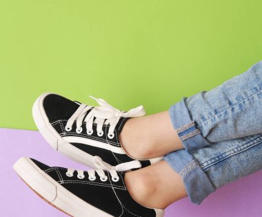 Renkli arka planda şık spor ayakkabılı kadın bacakları. Mor ve yeşil arka planda moda ayakkabılar.