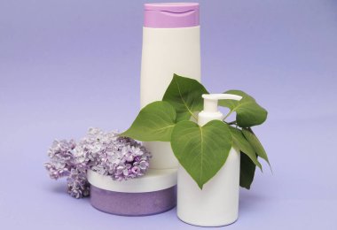 Arka planda leylak olan bir grup kozmetik şişesi. Yüz fırçası, jöle banyosu ve krem mor arka planda leylak çiçekleri.