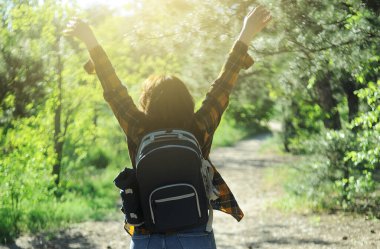 Sarı kareli gömlekli mutlu bir kadın seyahat çantasıyla ormanda vakit geçiriyor. Yaz tatili konsepti. 