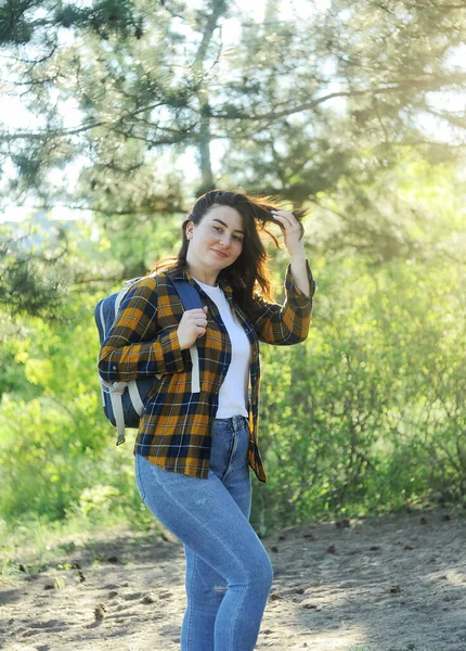黄色のチェック柄のシャツを着た笑顔の幸せな女性は 旅行バッグで森の中で時間を過ごします 夏休みのコンセプト — ストック写真