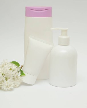 Beyaz bir zemin üzerinde kozmetik ürünü olan üç şişe leylak çiçekli.. 