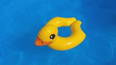 Mavi yüzme havuzunda, güneşten gelen su yüzeyi olan sarı plastik ördek.