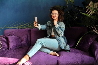 Gülümseyen kıvırcık kadın ev içinde selfie çekiyor.