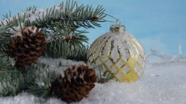 İyi yeni yıl ruhu. Karda Noel ağacı dalları. Noel ağacının dalında beyaz ve altın bir top. Işıklar. 4K 'da çekilmiş.
