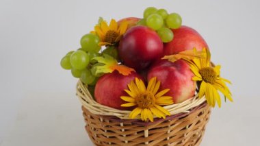 Hasır sepette taze meyveler ve beyaz arka planda çiçekler. Elma, üzüm, şeftali. 4K