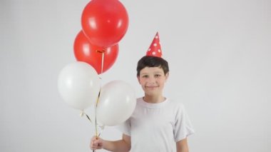 Doğum günü. Kırmızı doğum günü şapkalı bir çocuğun portresi. Kırmızı ve beyaz balonlar. 