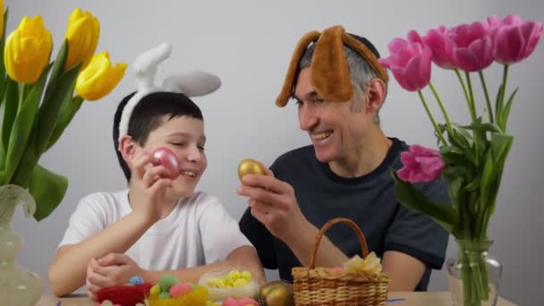 イースターエッグとウサギの耳を持つ面白い幸せな赤ちゃんの男の子 パパと息子はイースターの準備をしてる — ストック動画