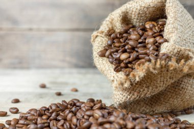 Ahşap bir arka planda çuval içinde kavrulmuş kahve. Kahve çekirdekleri ahşap bir zemine döküldü. Kahve işi. Kahve koleksiyonu. Kopyalama alanı