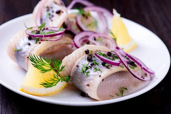Biber, otlar, tuz ve limon üzerinde beyaz seramik plat ile ringa balığı