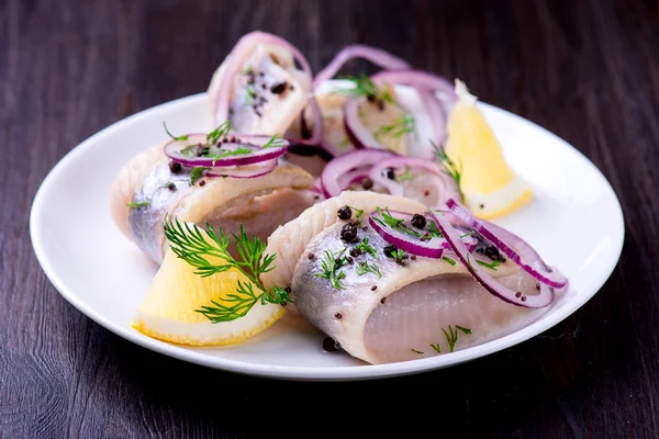 Biber, otlar, tuz ve limon üzerinde beyaz seramik plat ile ringa balığı